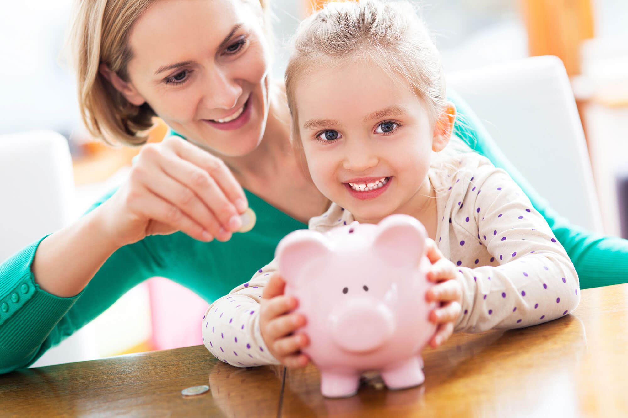 Photo of a Small Child and Woman putting coins into a Piggy Bank